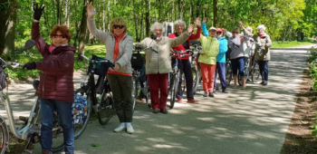 groepsfoto van oudere mensen in sportieve kleding buiten op een pad met fiets in de hand