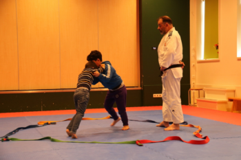 Twee kinderen krijgen judoles op een sportmat binnen een rode cirkel