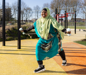 Een vrolijke vrouw met hoofddoek doet oefeningen met gewichtjes op een openbare beweegplek