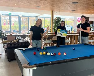 Een man en vrouw bij een pooltafel; de middelste heeft een cheque van 500 euro in haar handen