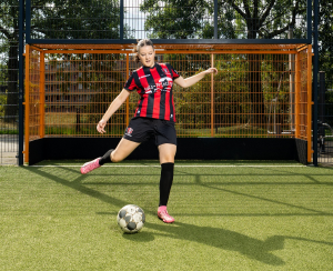 Bente, net voordat ze tegen een bal trapt; achter haar een oranje met zwart doel