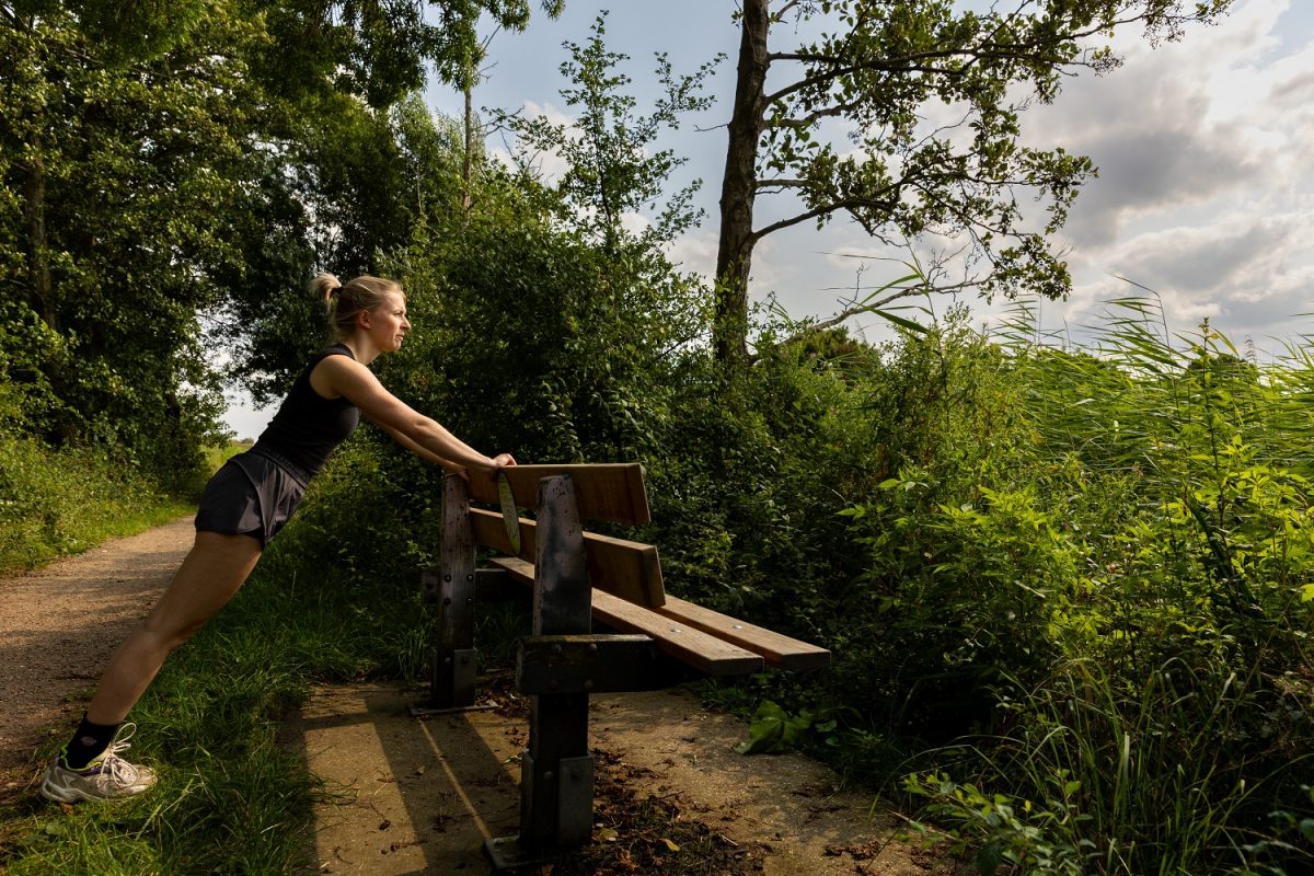 Vrouw doet stretchoefening bij bank in park