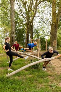 Mannen en vrouwen van verschillende leeftijden doen op toestellen oefeningen in bos