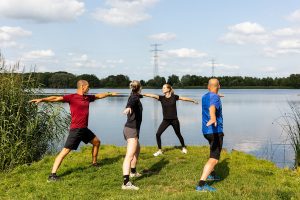 Twee mannen en vrouwen van verschillende leeftijden in stretchhouding aan het water