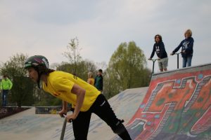 Jongere in actie op skatebaan, twee jongens kijken toe