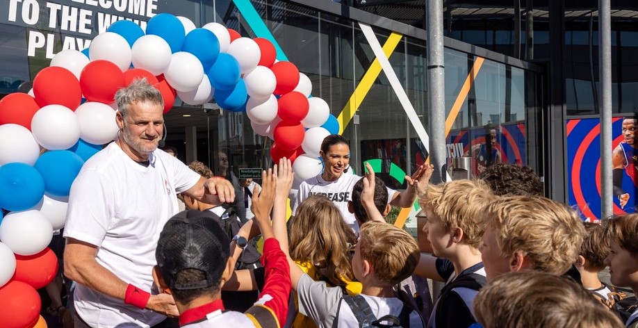 Een man en een vrouwen leiden kinderen de sporthal binnen