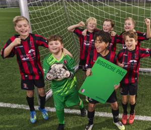 Groep jongens in voetbaltenues; de jongens juichen en een houdt een grote groene Bossche Pas vast