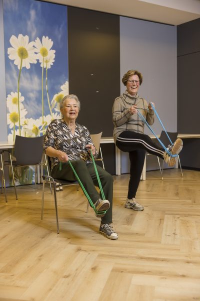 Gerda (91) en Marij (78) bewegen zich fit: Gerda zit in een stoel, Marij staat lachend naast haar