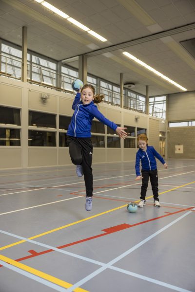 Vera (9) springt met een handbal in hand, terwijl zusje Vera (6) naar een bal op de grond kijkt