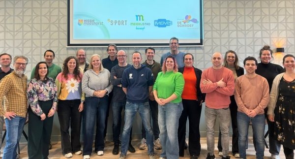 Een groep mensen voor een groot beeldscherm met daarop de namen van de samenwerkingspartners