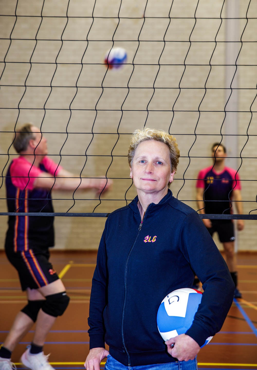 Op de voorgrond Petra Raams met bal in de hand; op de achtergrond twee volleyballers