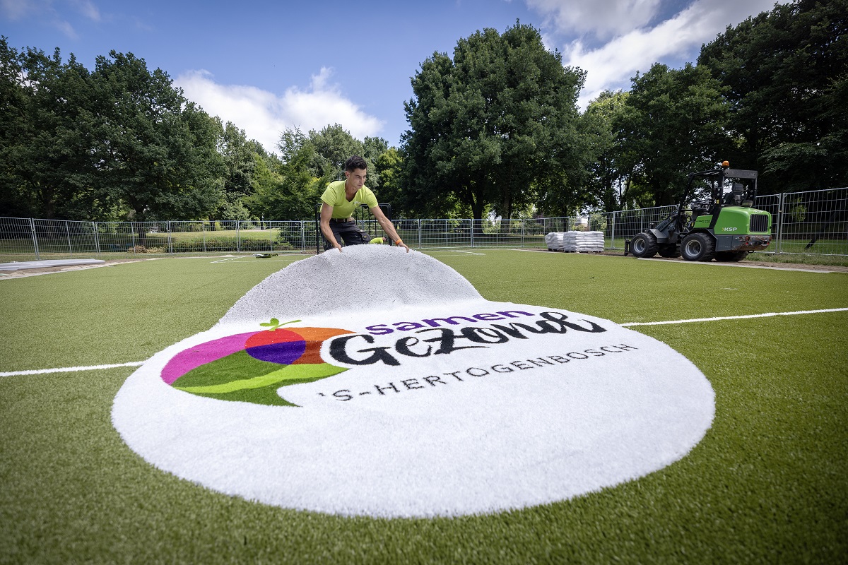 Man sleept logo van Samen Gezond 's-Hertogenbosch naar de juist plek op voetbalveld.