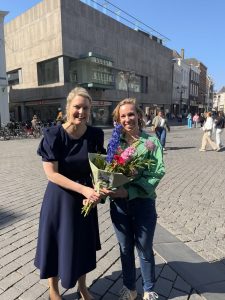 Vrijwilliger Kim krijgt op de Bossche Markt bloemen van wethouder Marianne van der Sloot