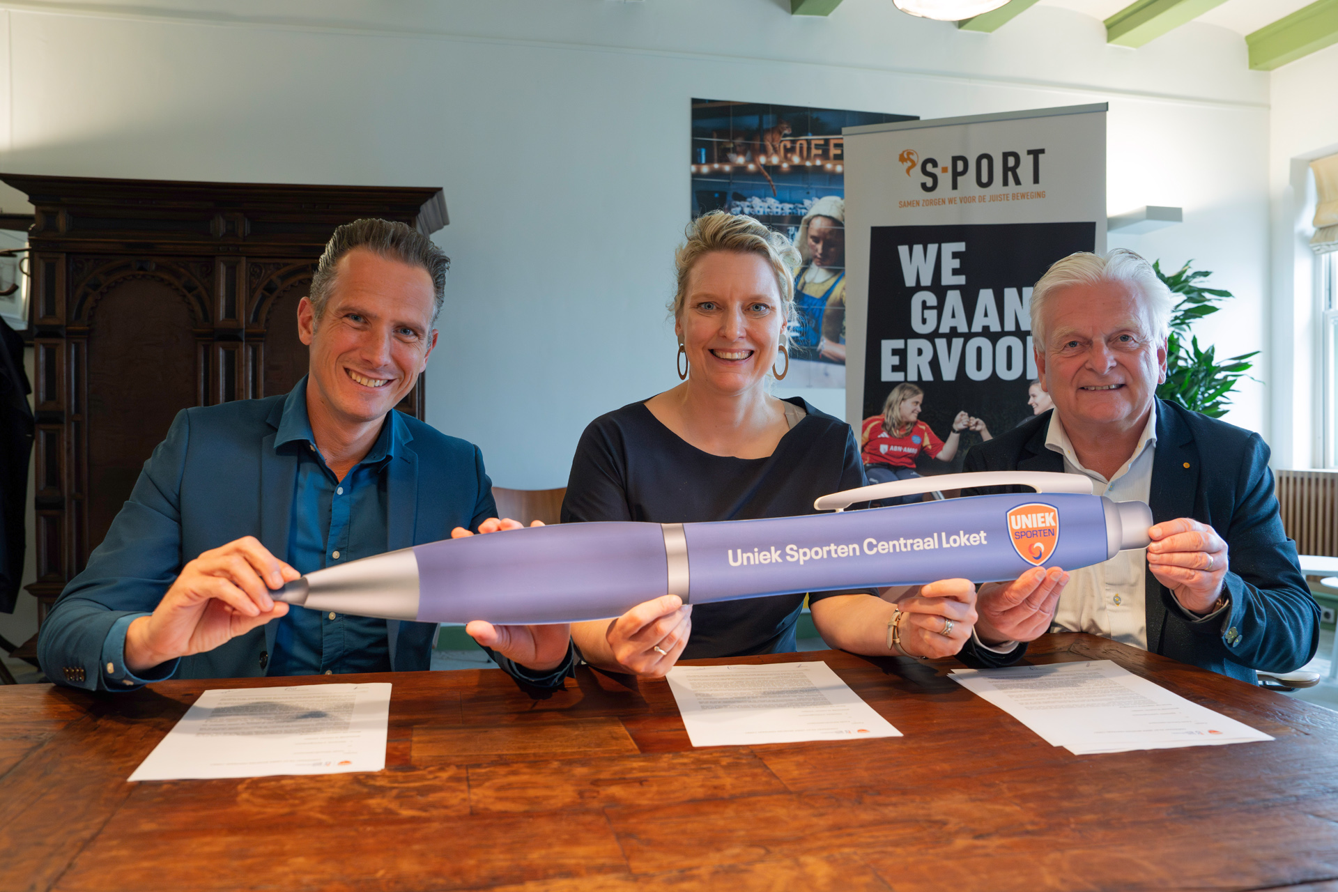 Wethouders Pieter Paul Slikker en Marianne van der Sloot en Uniek Sporten-directeur Nike Boor houden pen vast met tekst Uniek Sporten Centraal Loket