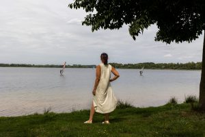 Vrouw met hand in zij kijkt uit over Engelermeer, twee surfers op achtergrond