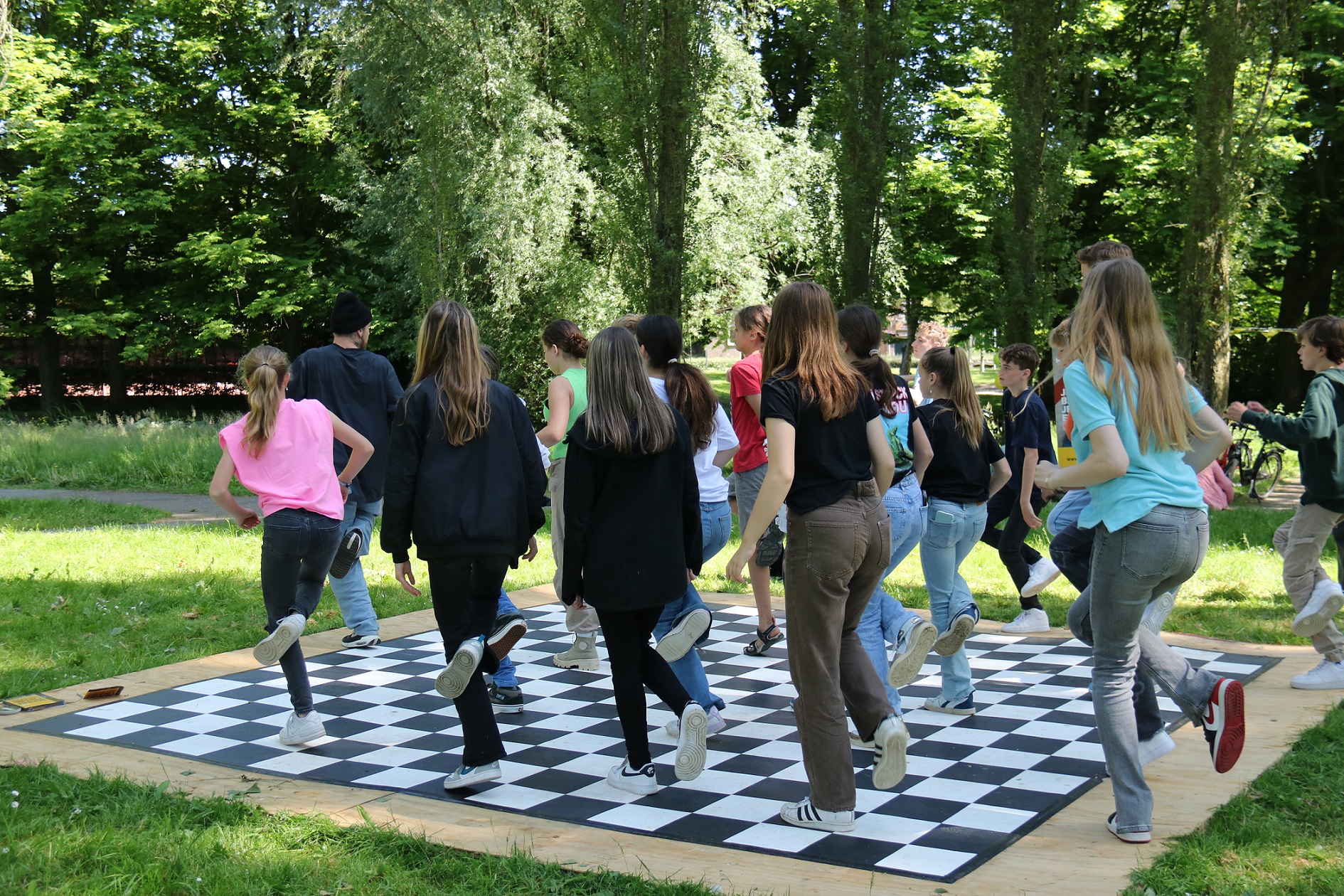 Jongeren dansen buiten in het groen op een zwart-wit-geblokte vloer