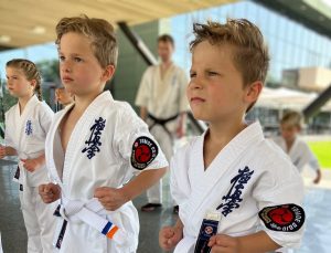 Drie jonge kleuters in witte karatepakken kijken gefocust