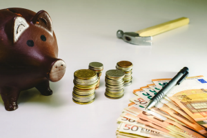 Geld (losgeld en briefjes), een pen, een hamer en een spaarvarken op witte tafel