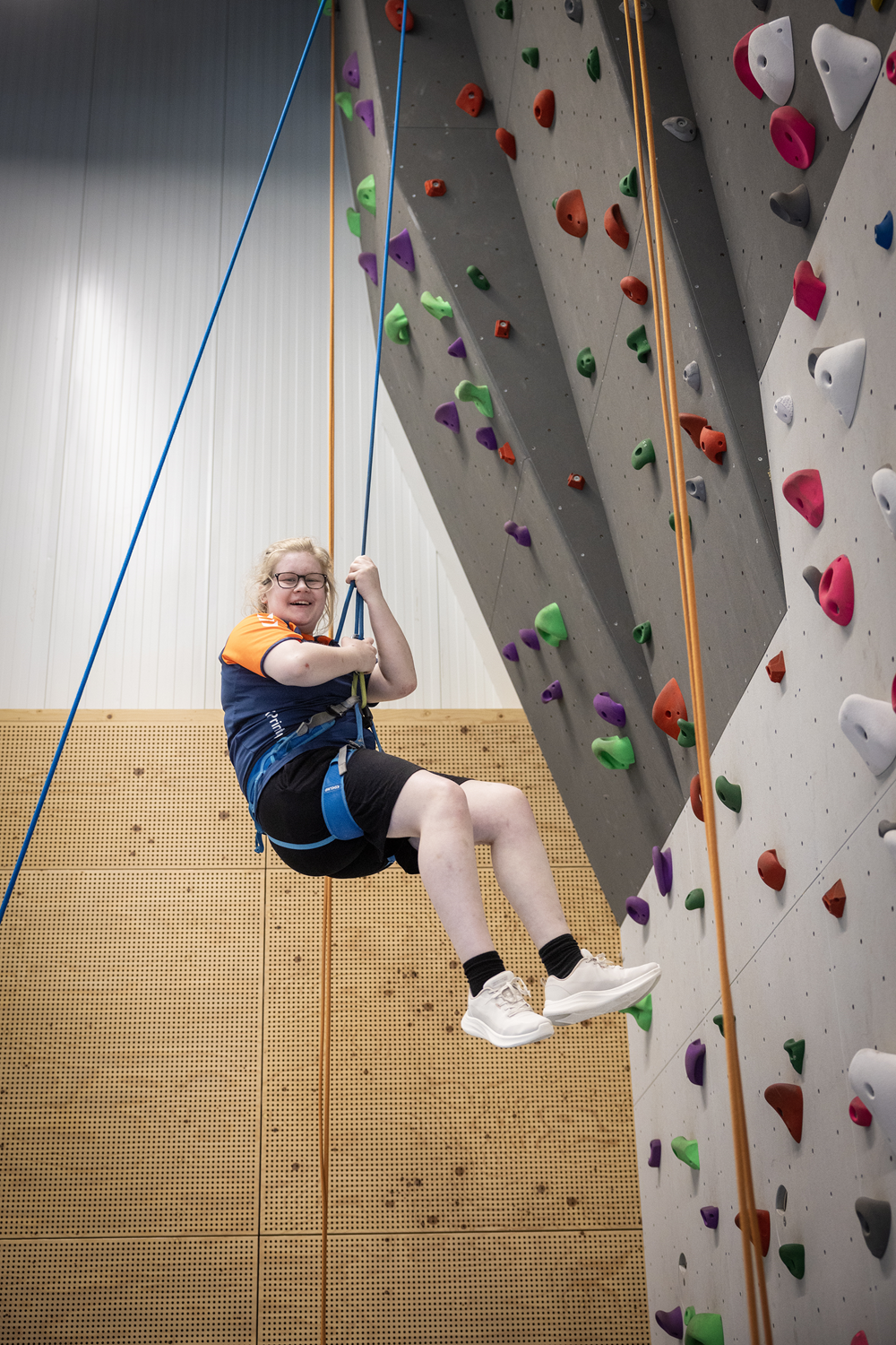 Lachende vrouw hangt aan zekeringstouwen bij klimwand