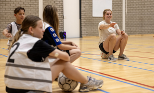 Jongeren zittend op een belijnde vloer in sporthal