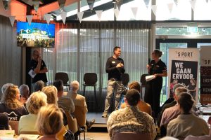 Vrouw interviewt man voor een groep zittende toehoorders